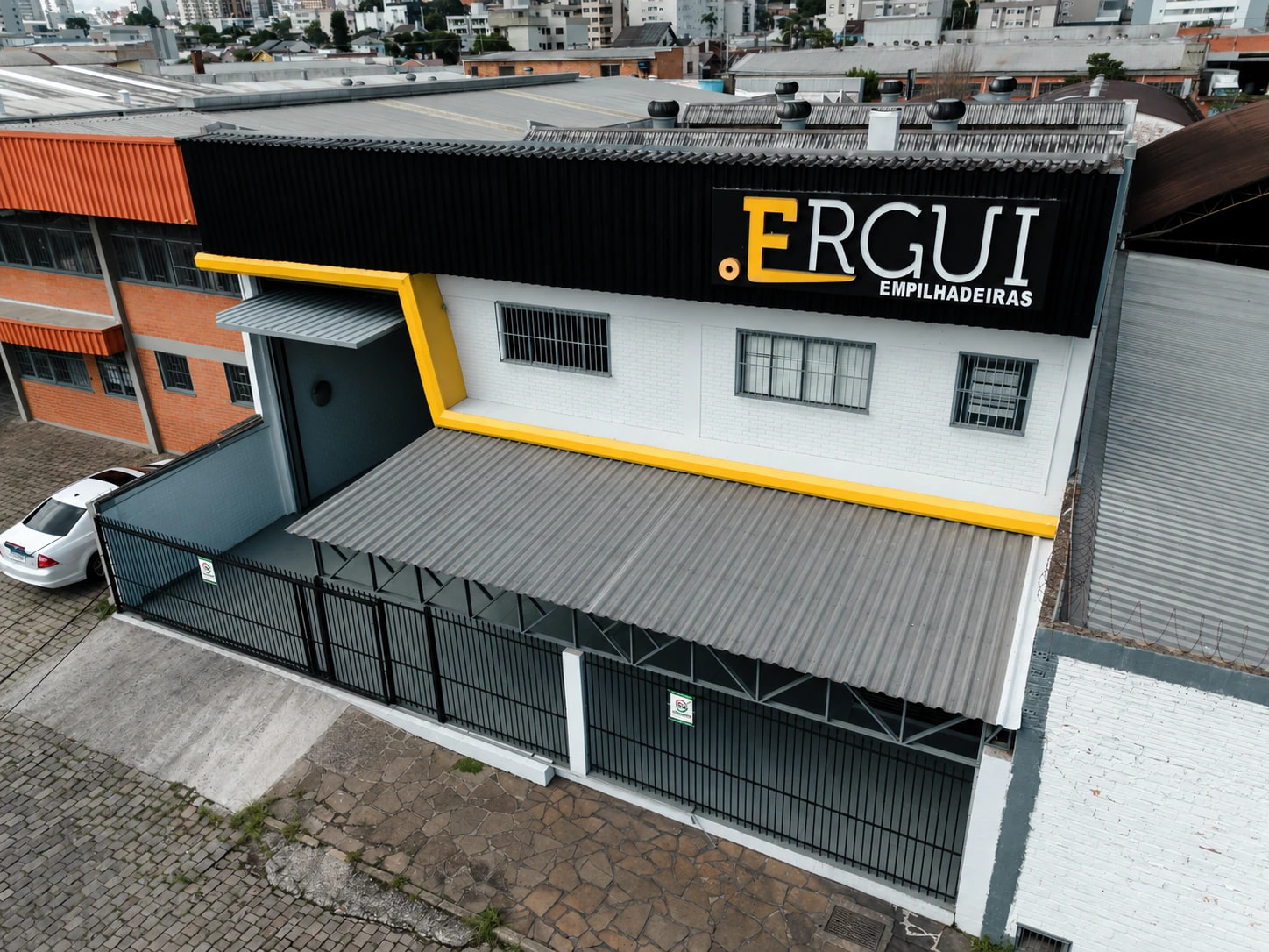 Fachada e acesso da Ergui em Caxias do Sul, com o letreiro da empresa; fotografia tratada por IA.