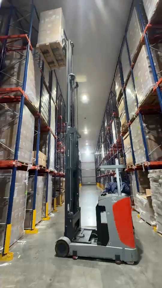 Empilhadeira retrátil com operador e palete de caixas elevado em corredor de armazenagem.